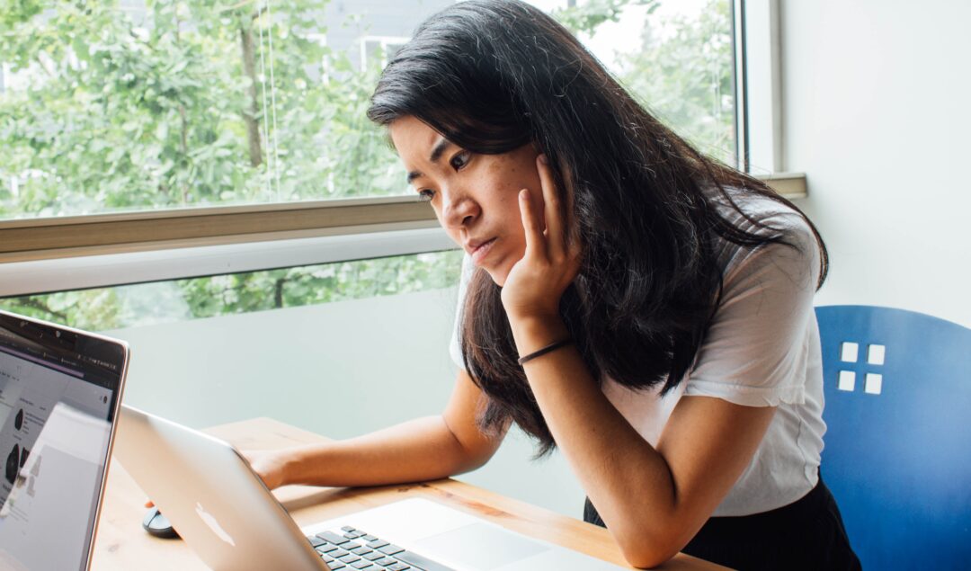 Asian woman looking at laptop with pensive expression