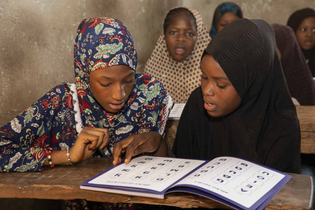 Two school girls reading from an ADLAM book