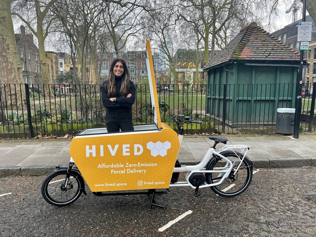 Murvah Iqbal an Asian woman with long black hair with blonde tips standing by a Hived electric parcel delivery bike in London.
